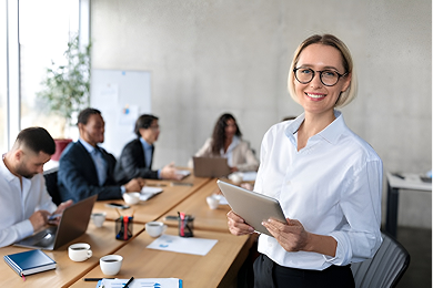 Una donna che guida una riunione con un tablet, mentre i colleghi lavorano su laptop